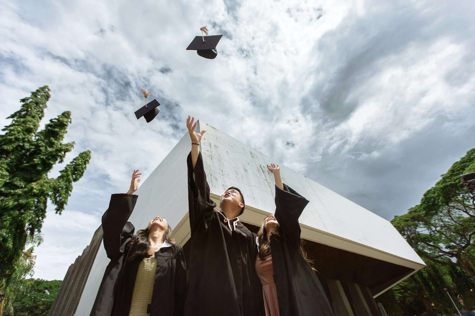 Graduates joyfully tossing caps in air outdoors against a modern building.